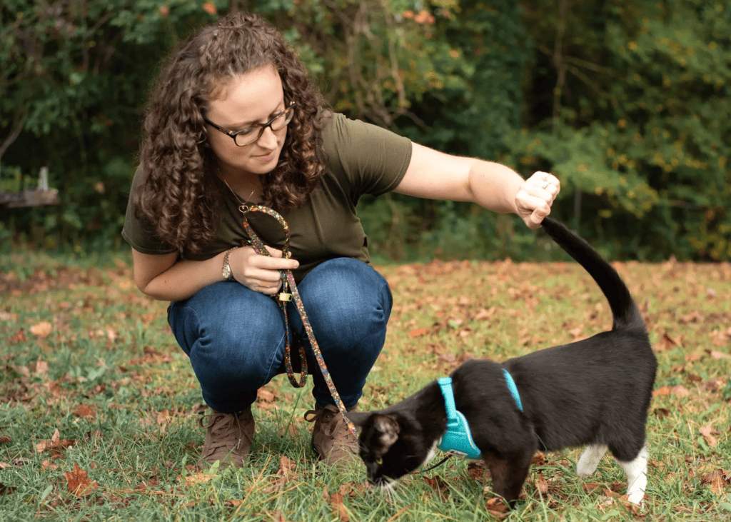 woman kneeling and petting black and white cat outside on a harness and leash