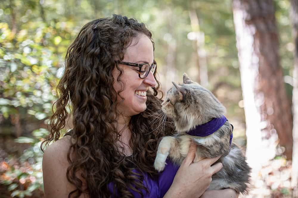 Woman with a cat in a harness in the woods