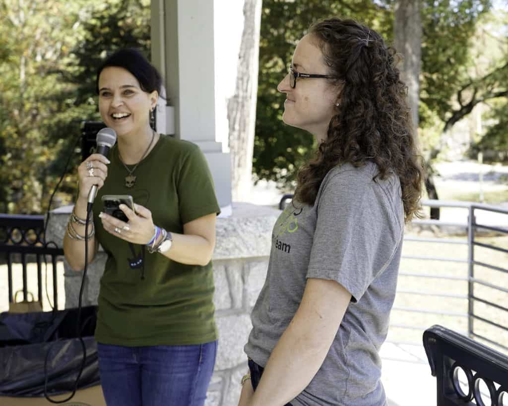 two women standing together, one is talking into a microphone and the other is smiling